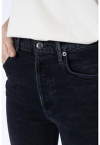 Jeans de mezclilla negra con una textura suave, con un cierre de botón plateado, bolsillos cosidos y un diseño ajustado en la cintura.