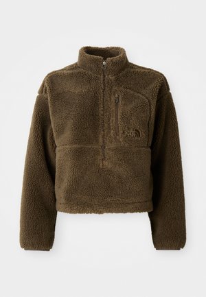 Bruine fleecjas met een hoge kraag, een halve rits aan de voorkant en een borstzak; heeft een gestructureerde stof en een logo op de voorkant.