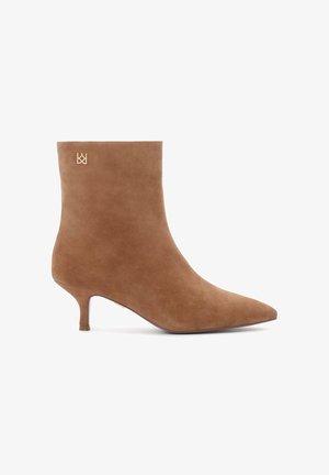 Bottines en suède marron avec un bout pointu, dotées d'un petit talon kitten et d'un accent logo doré près du haut. Texture lisse dans l'ensemble.