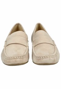 Beige semišové mokasíny se šitým švem, kulatou špičkou a páskem přes přední část. Měkká textura a plochá podrážka.