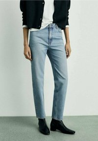 Jean taille haute bleu clair, coupe droite, en denim. Associé à un cardigan noir et des bottines noires. Texture lisse.