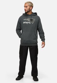 Sudadera color gris carbón con el logo "PATRIOTS", capucha con cordones, bolsillo frontal y puños acanalados; combinada con pantalones cargo negros y zapatillas.