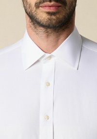Witte button-up shirt met een klassieke kraag, een gladde textuur en parelachtige knopen. Close-up van de voorkant van het shirt.