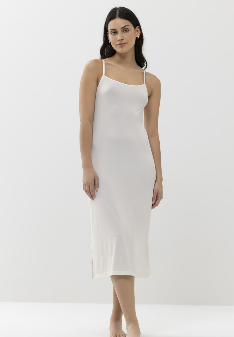 Robe de dessous blanche, arrivant au genou, avec des bretelles fines, fabriquée en tissu lisse. Présente un décolleté droit et une fente sur le côté pour faciliter les mouvements.