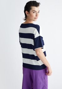 Top in maglia a righe blu navy e bianco, con maniche corte e orlo a coste. Il retro presenta un sottile dettaglio perforato vicino al fondo.