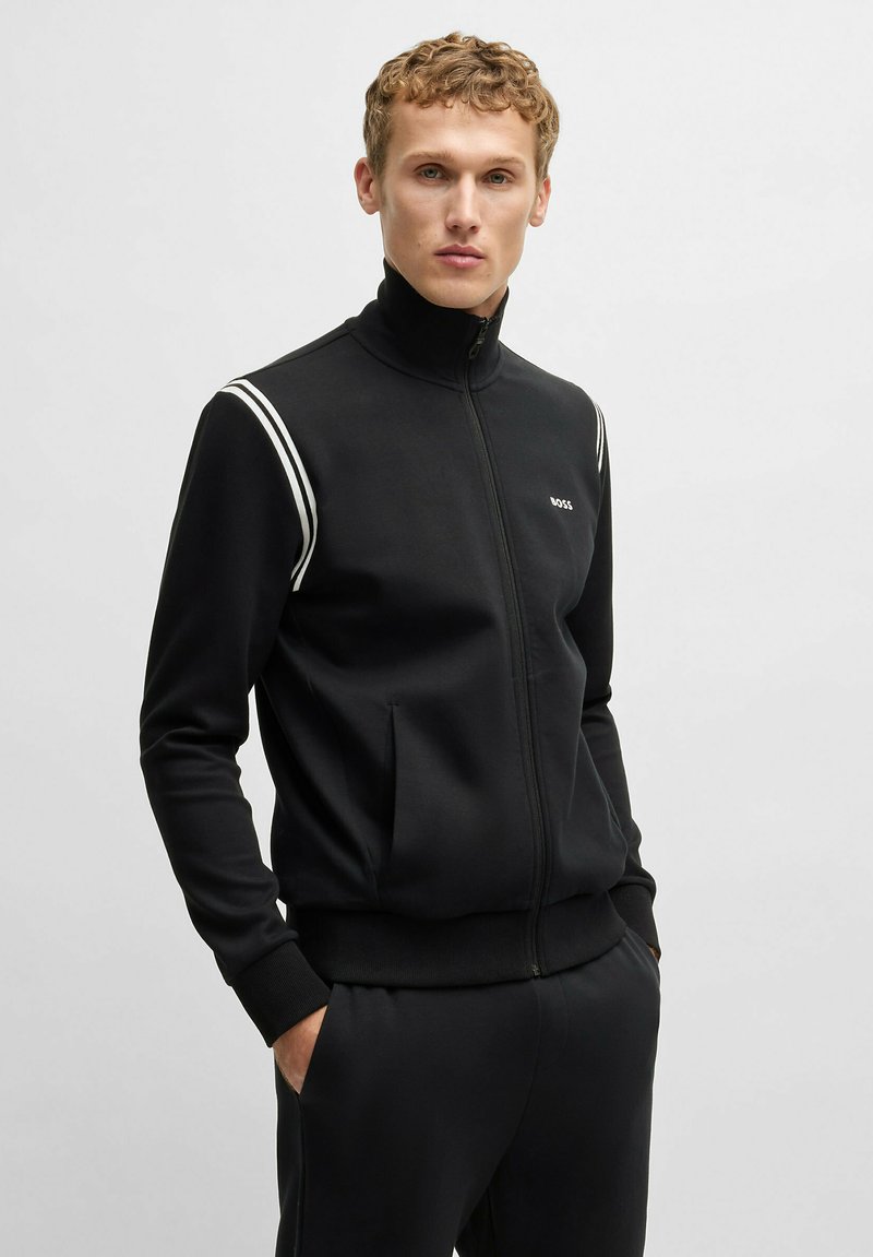 Schwarze Zip-Up Trainingsjacke mit hohem Kragen, weißen Schulterstreifen und glattem Stoff. Verfügt über Seitentaschen und ein tailliertes Design.