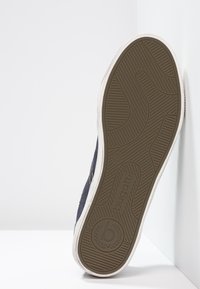 Námořnické plátěné tenisky s flexibilní gumovou podrážkou s texturovaným hnědým vzorem a bílou mezipodešví. Logo viditelné na spodní části.