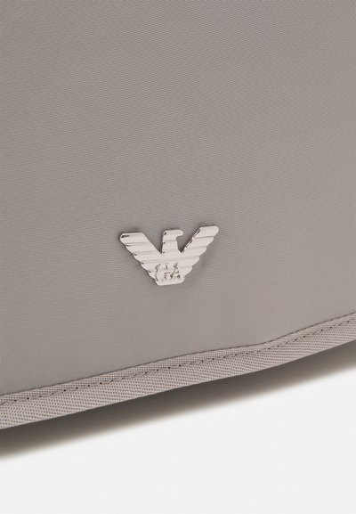 Borsa di tessuto grigio caratterizzata da una superficie texture sottile, con un'emblema in tono argento che mostra una lettera "W" stilizzata e "GA" in basso.