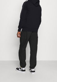 Sudadera con capucha azul marino con rayas laterales blancas, combinada con pantalones cargo negros con diseño de múltiples bolsillos y zapatillas negras de Nike.