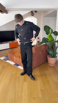 Jeans de mezclilla negros de corte regular, llevados con un sudadera negra que presenta patrones triangulares, situados en una sala de estar.