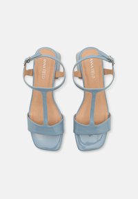 Sandali in pelle verniciata blu con design aperto, punta quadrata, cinturino alla caviglia e soletta color sabbia. Presentano una silhouette elegante e minimalista.