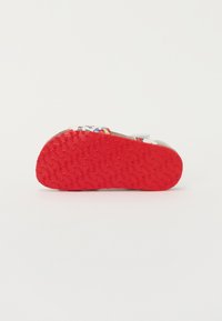 Sandals with a textured, red rubber outsole, featuring a decorative printed upper in various colors and patterns, secured by adjustable straps.