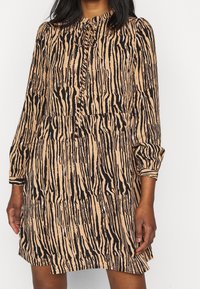 Elävä eläinkuosikuvioinen mekko beigen ja mustan sävyissä, jossa on pitkät hihat, pyöreä pääntie, kermaviilitettu vyötärö ja nappiyksityiskohta kauluksessa.