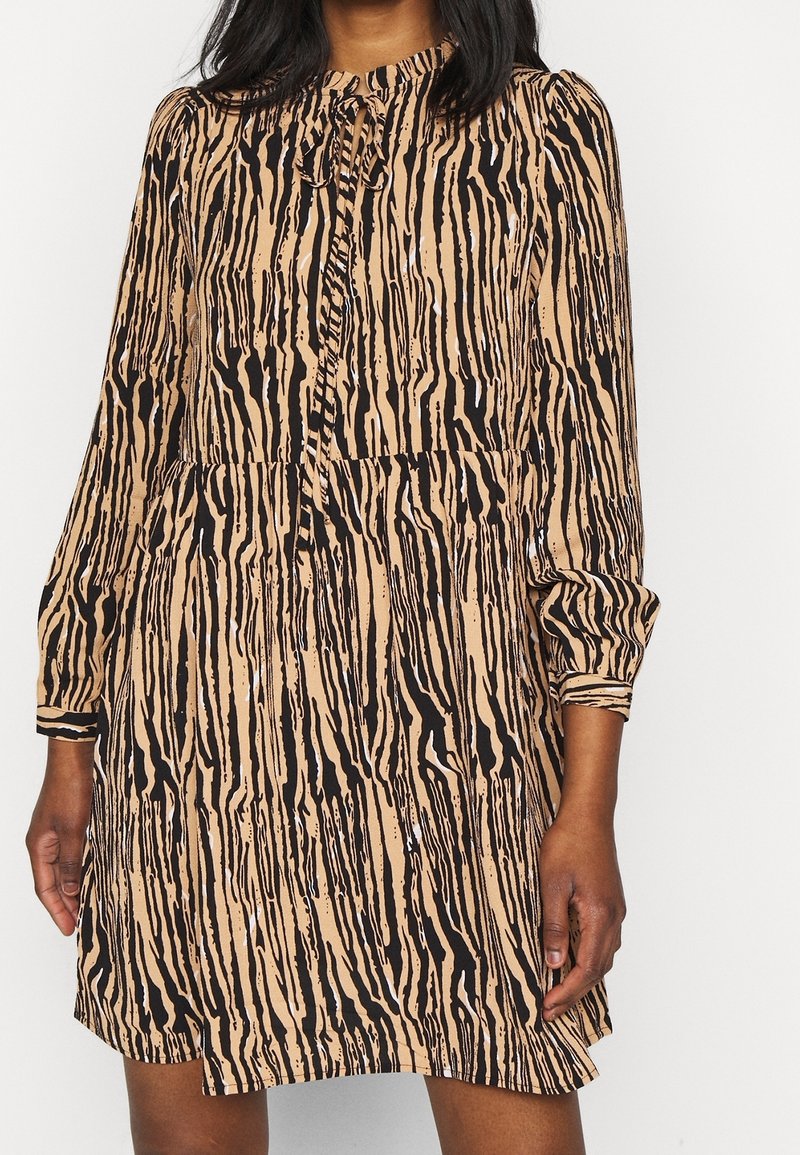 Elävä eläinkuosikuvioinen mekko beigen ja mustan sävyissä, jossa on pitkät hihat, pyöreä pääntie, kermaviilitettu vyötärö ja nappiyksityiskohta kauluksessa.