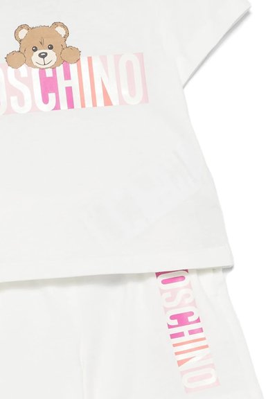 Completo di maglietta bianca e pantaloni corti con una grafica di un orso e il logo "Moschino" stampato in un gradiente di rosa su un tessuto dalla texture morbida.