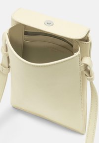 Kremowa skórzana torba na ramię o minimalistycznym designie; posiada zapięcie na zatrzask, wewnętrzną kieszeń oraz teksturowane wykończenie zewnętrzne.