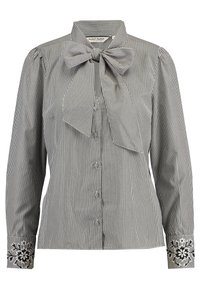 Camicia a righe in bianco e nero, caratterizzata da un colletto con fiocco e da polsini ricamati con fiori. Realizzata in tessuto leggero.