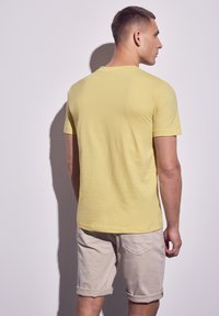 Žluté bavlněné tričko s kulatým výstřihem a krátkými rukávy, doplněné o ohrnuté khaki šortky. Jednoduchý design, strukturovaná tkanina.