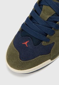 Αθλητικό παπούτσι με navy μπλε δίχτυ και άνω μέρος από σουέντ, με ελιτζέν πράσινες λεπτομέρειες, στρογγυλά κορδόνια και ένα μικρό κόκκινο λογότυπο κοντά στη μύτη.