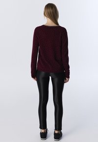Pull bordeaux avec un motif texturé, manches longues et ourlet côtelé, accompagné de leggings noirs brillants et de baskets noires texturées.