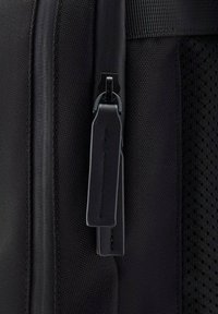 Bolsa de tela negra con cremallera suave, acentuada por un tirador de cuero y un panel de malla, destacando la durabilidad y un acabado texturizado.