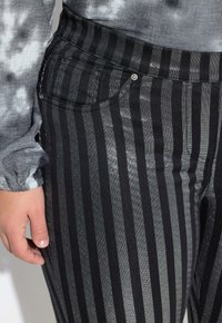 Pantalon rayé noir et gris avec une légère brillance, doté d'une poche avant, d'une coupe ajustée et d'un matériau texturé. Tissu doux visible.