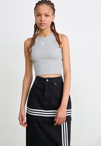 Pelēks ribots crop tops ar Adidas logotipu, savienots ar melnu džinsu svārku ar baltām horizontālām svītrām apakšmalē un sānos.