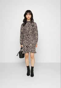Vestido de mangas compridas com um padrão de zebra preto e bege, cintura ajustada e barra com ruffles; combinado com uma bolsa preta e botas de tornozelo.