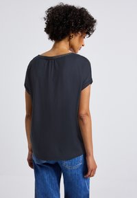 Blouse noire à manches courtes avec un col rond, présentant un motif texturé le long du col et une coupe décontractée pour plus de confort.