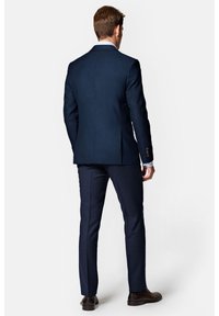 Granatowy, dopasowany garnitur z taliowaną marynarką i spodniami bez kantów, wykonany z teksturowanej tkaniny, z subtelnymi przeszyciami i dopasowanymi ciemnymi butami.