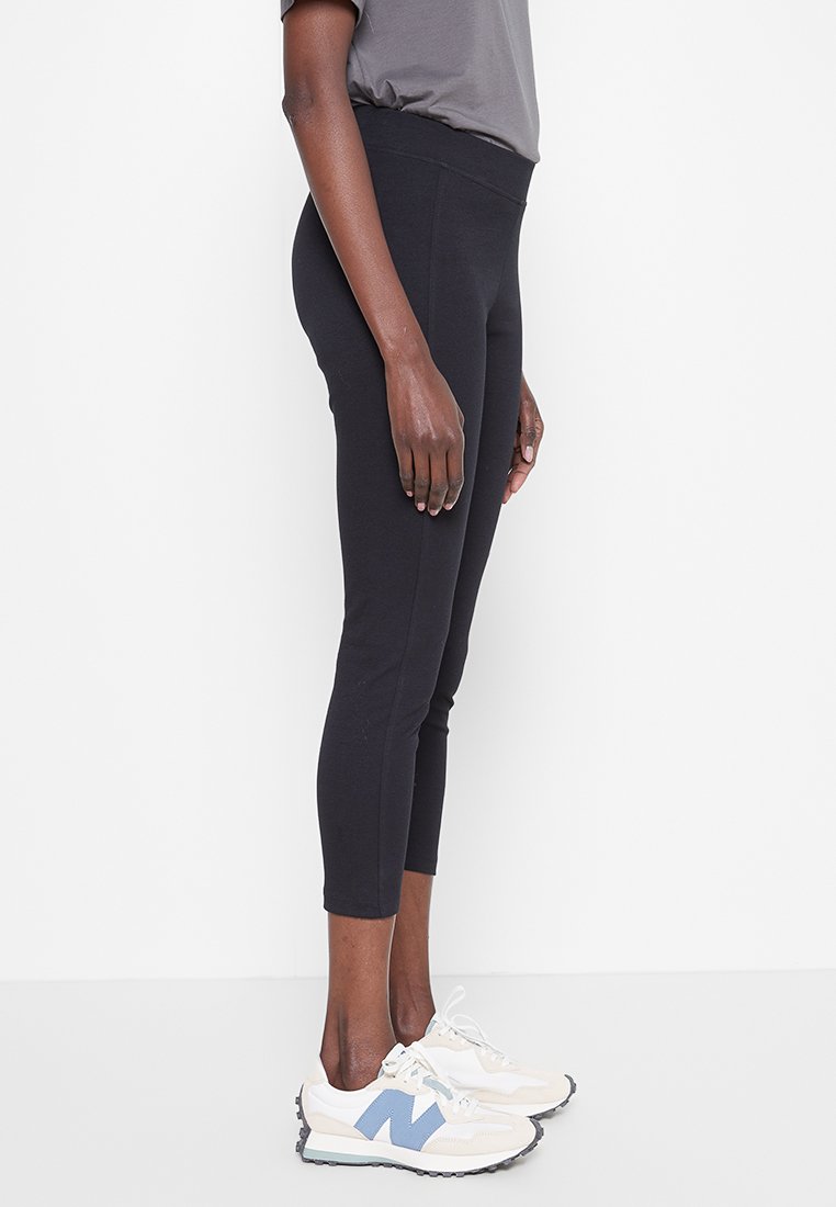 Leggings negras de cintura alta con una textura suave y un diseño ajustado, acompañadas de zapatillas ligeras con acentos azules y detalles blancos.