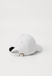 Cască de baseball din bumbac alb, cu vizieră curbată, curea ajustabilă la spate și un mic accent metalic sub formă de cataramă. Design simplu, fără modele.