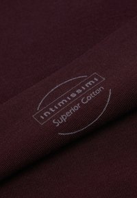Bordowy materiał bawełniany o prążkowanej fakturze, z białym logo nadrukowanym w pobliżu krawędzi, które brzmi "intimissimi Superior Cotton".