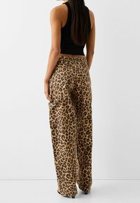 Luipaardprint broek met brede pijpen in bruin en zwart, met een hoge taille en zijzakken, gemaakt van lichte stof.