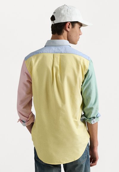 Camisa multicolorida em algodão; apresenta secções em amarelo pastel, rosa, verde e azul; corte descontraído com mangas dobradas e barra curva.