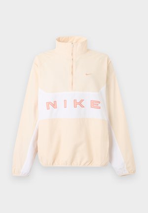 Beige og hvid Nike pullover med kvart lynlås, elastiske ærmegab og kant, stor lyserød "NIKE" tekst på tværs af brystet og lille swoosh logo på venstre bryst.