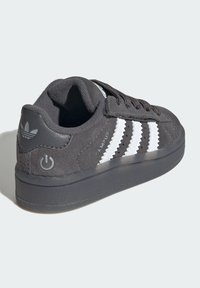 Black Adidas Campus sneaker with white zigzag stripes, lace-up design, padded collar, and logos on heel and side, angled to show outer side and heel.