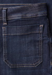Poche de jean en denim bleu foncé avec coutures orange et passants de ceinture sur un jean plié.