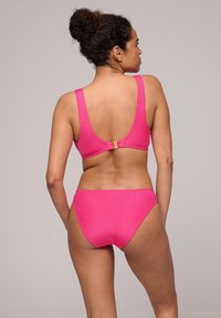 Różowy bikini w prążki z niskim dekoltem, szerokimi ramiączkami i złotym zapięciem na górze; dopasowane majtki o niskim stanie.