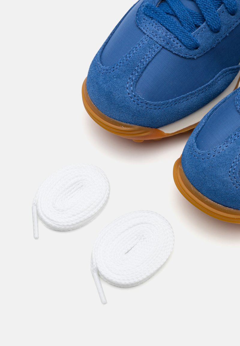 Zapatillas azules de ante y nylon, con suela de goma, y dos cordones de algodón blancos colocados en la parte inferior.