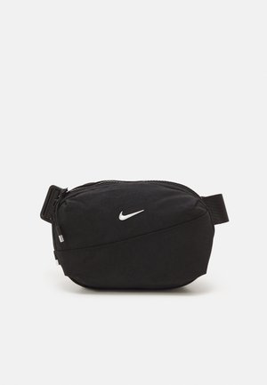 Sac banane Nike noir avec une texture lisse, un design courbé et une fermeture éclair à l'avant. Il présente un logo blanc et une sangle réglable.