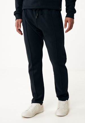 Black jogger pants made of soft fabric. Features an elastic waistband with drawstring, side pockets, and tapered leg design. Paired with white sneakers.