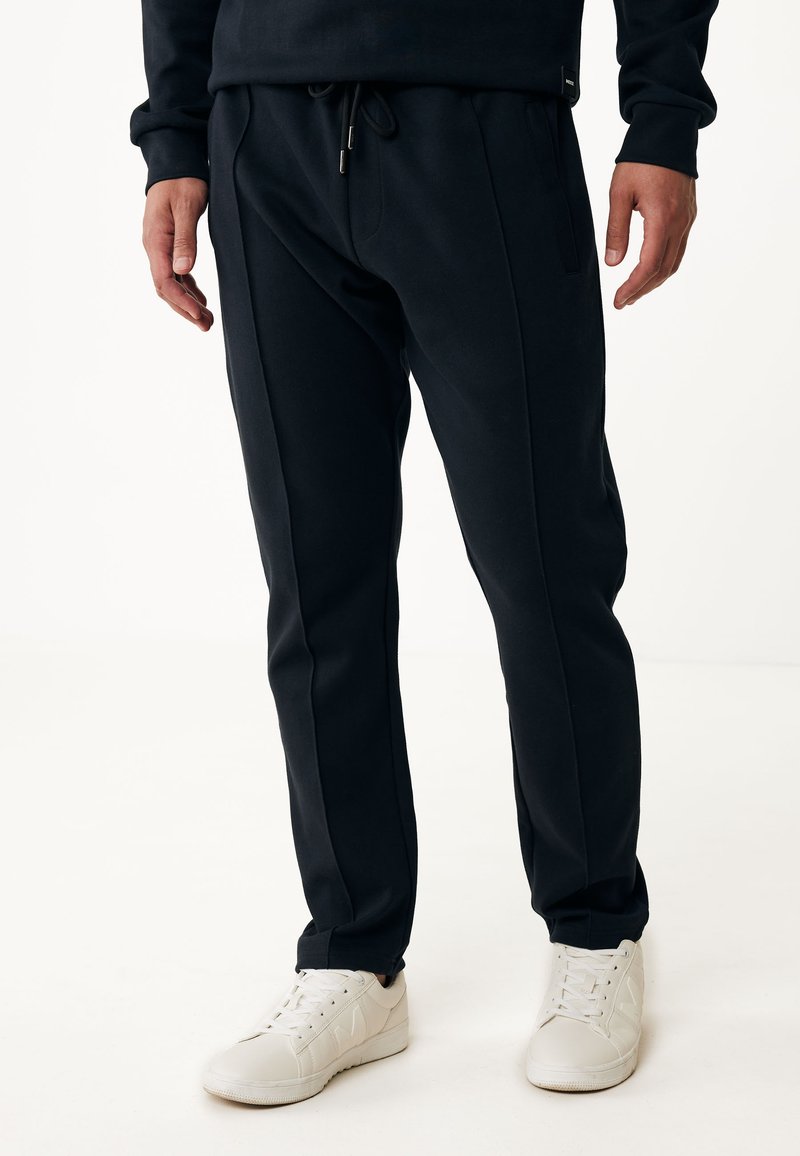 Pantalones jogger negros de tejido suave. Cuentan con una cintura elástica con cordón, bolsillos laterales y un diseño de pierna ajustada. Combinados con zapatillas blancas.