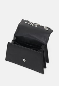 Svart läderhandväska med en metallisk logodetalj och ett tryckknappslås. Inuti finns flera fack för organisation.