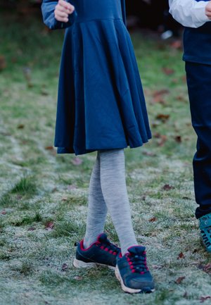 Blå kjole med en svajende nederdel, grå leggings og mørke sneakers med røde accenter. Græs og blade synlige i baggrunden.