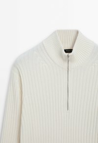 Pull en tricot côtelé blanc cassé avec une fermeture éclair demi-zip et un col haut replié, fabriqué en tissu doux et épais.