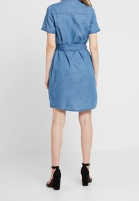 Denim-Shirtkleid mit kurzen Ärmeln, tailliertem Schnitt, leicht A-Linie und abgerundetem Saum. Aus einer weichen Textur und in hellblauer Farbe gefertigt.