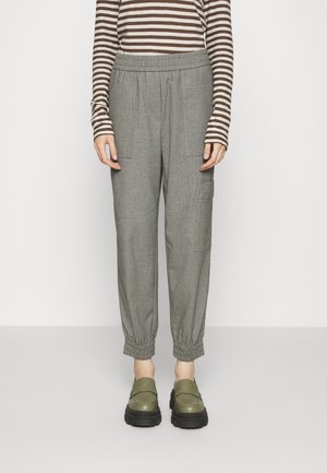 Personne portant un pantalon de jogger gris à taille élastique avec poches à l'avant et sur les côtés, un haut à manches longues rayé marron et blanc, et des chaussures compensées vert olive.