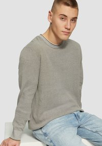 Szary sweter dzianinowy z okrągłym dekoltem, z teksturowanej tkaniny i długimi rękawami, zestawiony z jasnoniebieskimi dżinsami. Minimalistyczny design.