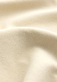 Detail měkké béžové žebrované látky s jemnými záhyby a jemnými vodorovnými texturami.